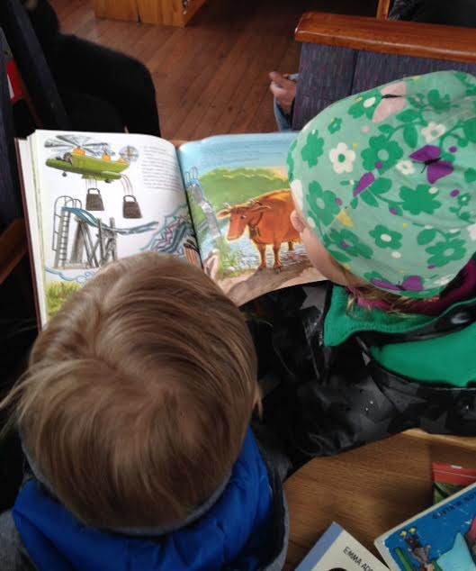 Två barn, ett med blommig mössa, läser i en barnbok om Mamma Mu.