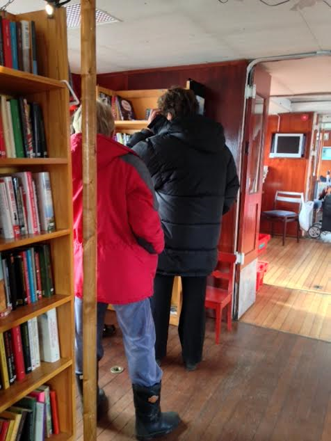 Två personer i röda och svarta jackor tittar på böcker i biblioteket på Bokbåten