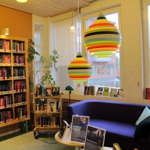 Biblioteksinteriör med blå soffa, bokhyllor och färgglada lampor
