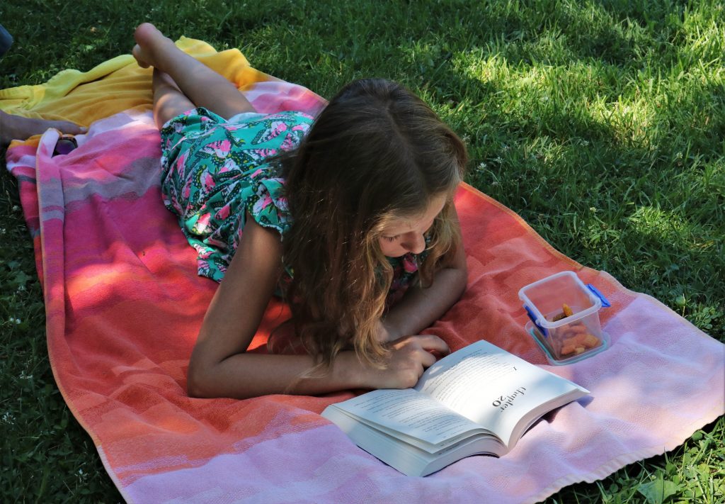 Flicka som läser på en filt i gräset.